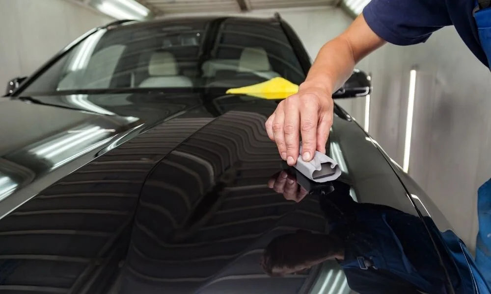 Detailing professional applying ceramic coating on a black car's surface, showcasing vehicle maintenance and protection techniques.