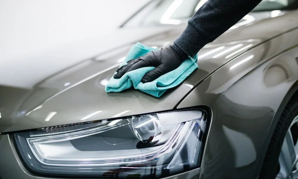 Person in black gloves cleaning car hood with microfiber cloth, emphasizing auto detailing and vehicle maintenance.