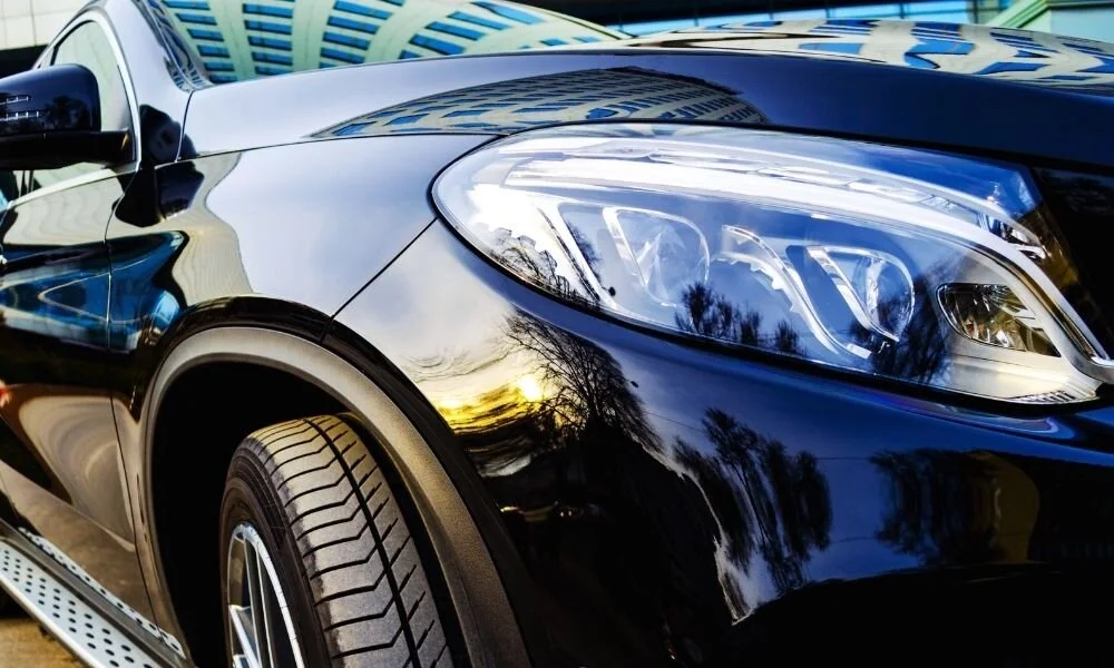 Black car exterior with gleaming headlights, showcasing reflections and detailing, relevant to car care and ceramic coatings.
