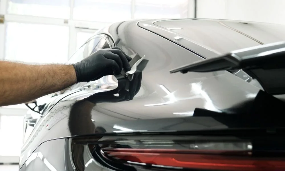 Person applying ceramic coating to a black car's rear, showcasing vehicle detailing and protection techniques.