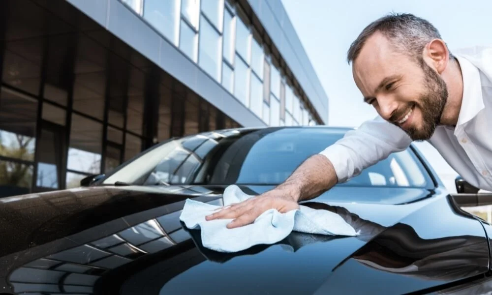 Man detailing a black car with a microfiber cloth, showcasing car maintenance and preparation for ceramic coating.