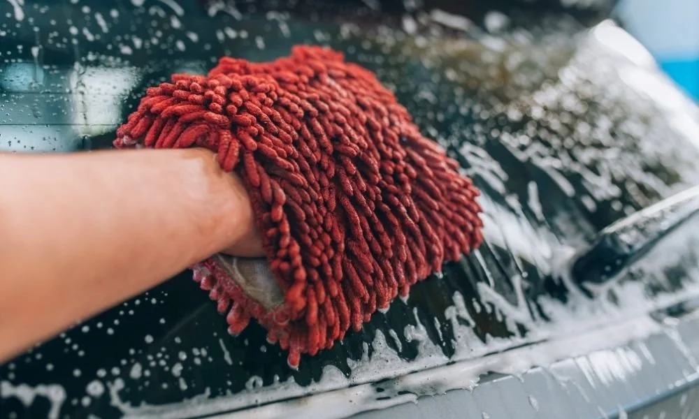Person using a microfiber wash mitt to clean a vehicle's surface, emphasizing automotive care and detailing services.