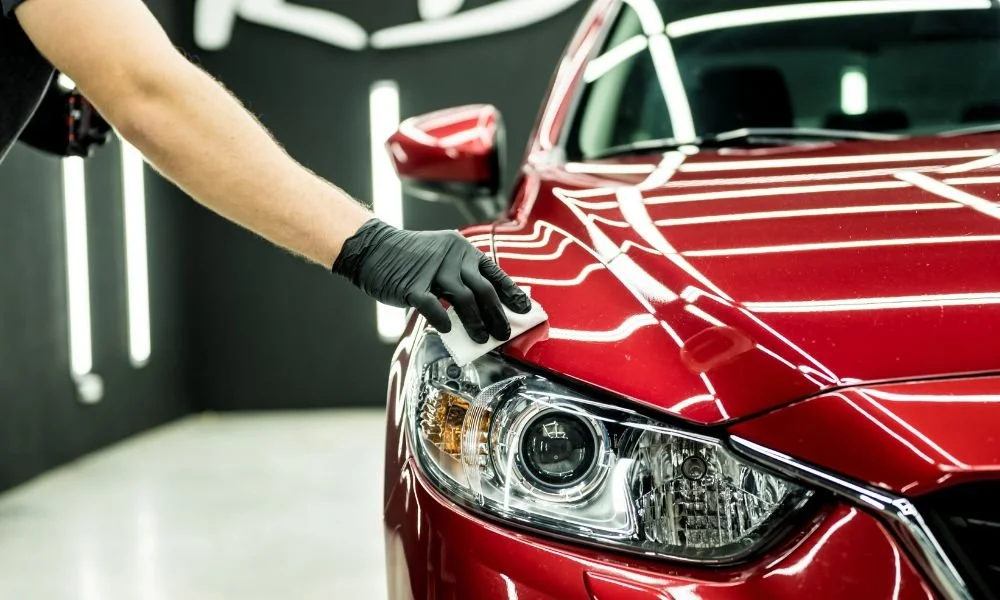 Person applying ceramic coating to a red vehicle, highlighting detailing techniques for maintaining car paint and enhancing vehicle appearance.