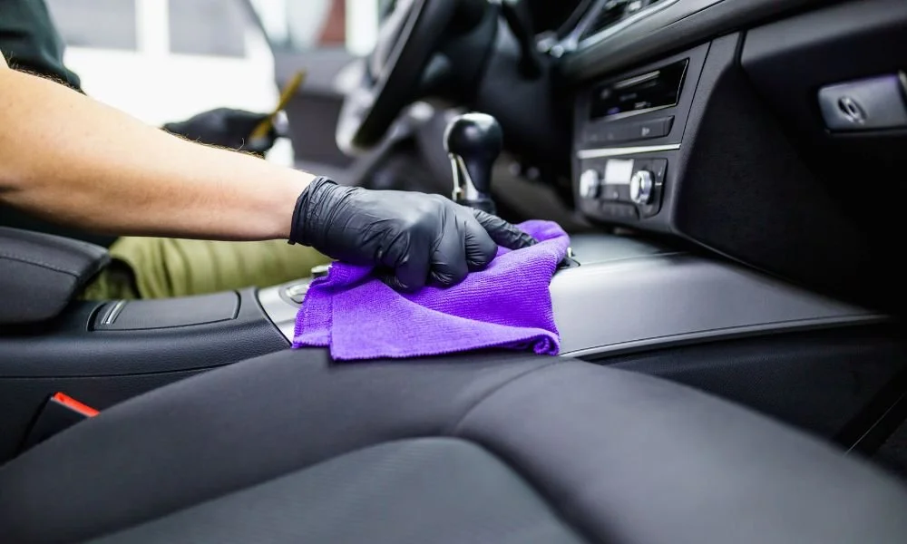 Person wearing gloves cleaning car interior with a purple microfiber cloth, highlighting auto detailing services offered by Owner's Pride.