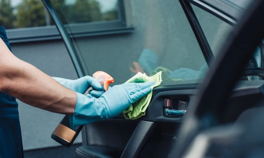 Person cleaning car interior with microfiber cloth and spray cleaner, emphasizing vehicle maintenance and detailing services.