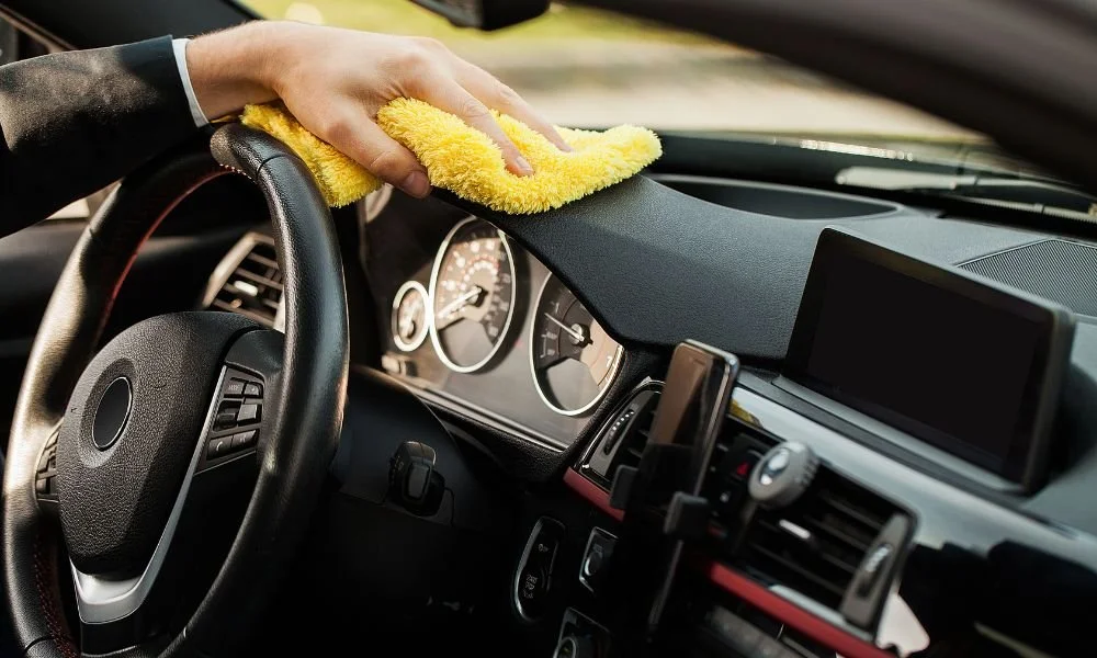 Person cleaning car dashboard with a yellow microfiber cloth, showcasing interior detailing for vehicle maintenance.