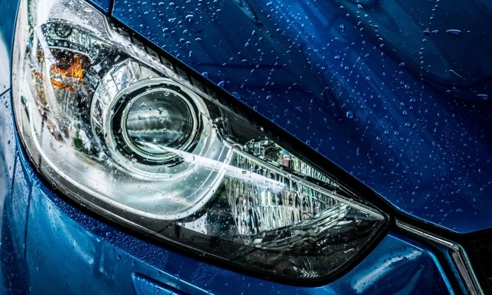 Close-up of a blue car's headlight with water droplets, emphasizing the importance of car washing and detailing for vehicle maintenance.