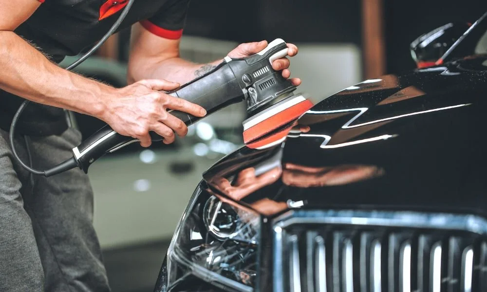 Person using a polishing machine on a black car hood, showcasing auto detailing techniques relevant to vehicle maintenance and protection.