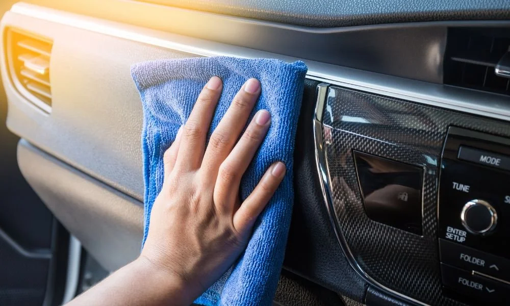 Person cleaning car interior dashboard with microfiber cloth, emphasizing vehicle detailing before summer.