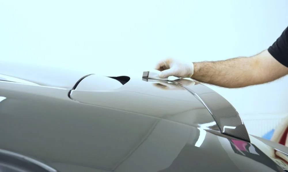 Person applying paint protection film on a vehicle's hood to enhance its appearance and protect against sun damage.