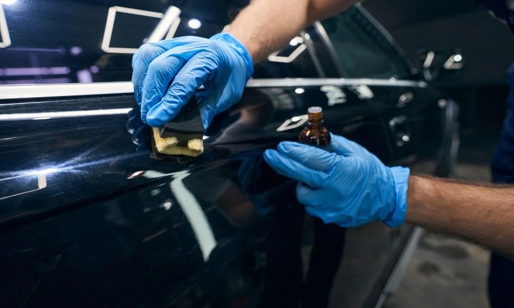 Detailing professional applying protective coating to car paint using a sponge and solution, emphasizing vehicle maintenance and protection from environmental damage.