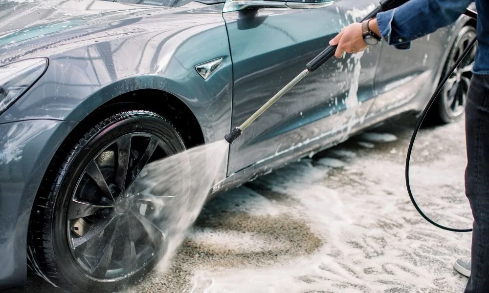Person using a pressure washer on a gray vehicle, illustrating effective car washing techniques related to auto detailing and maintenance.