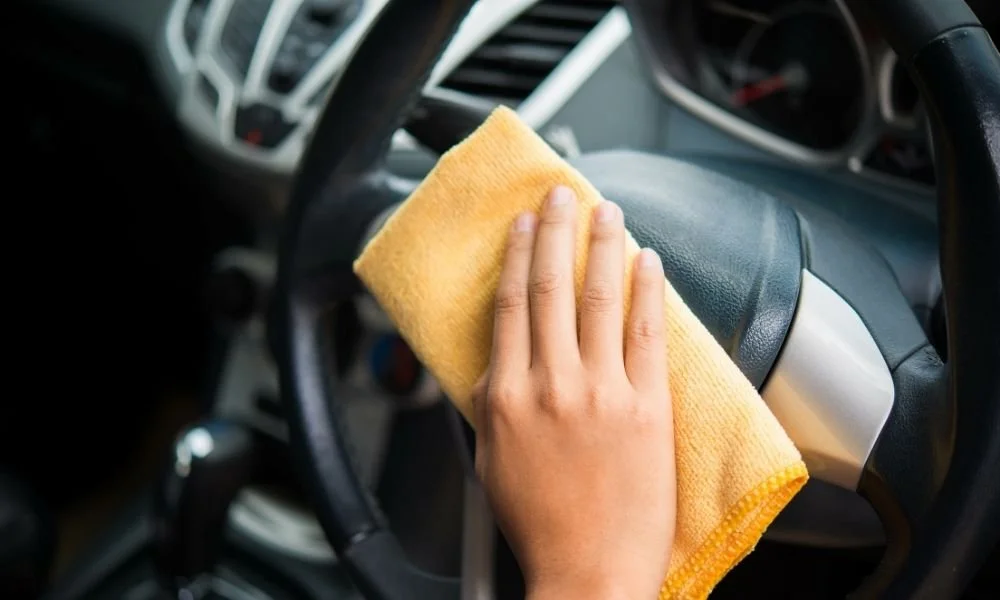 Hand cleaning the steering wheel of a car with a microfiber cloth, emphasizing the importance of detailed vehicle maintenance.