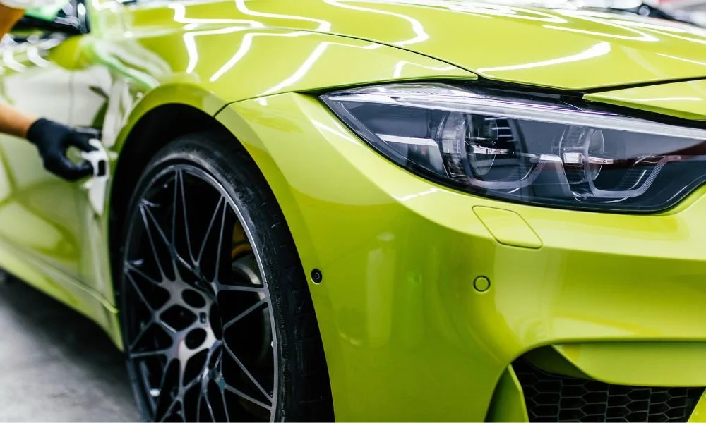 Detailing technician applying protective sealant on a vibrant green car, showcasing the importance of car detailing for vehicle maintenance and value preservation.