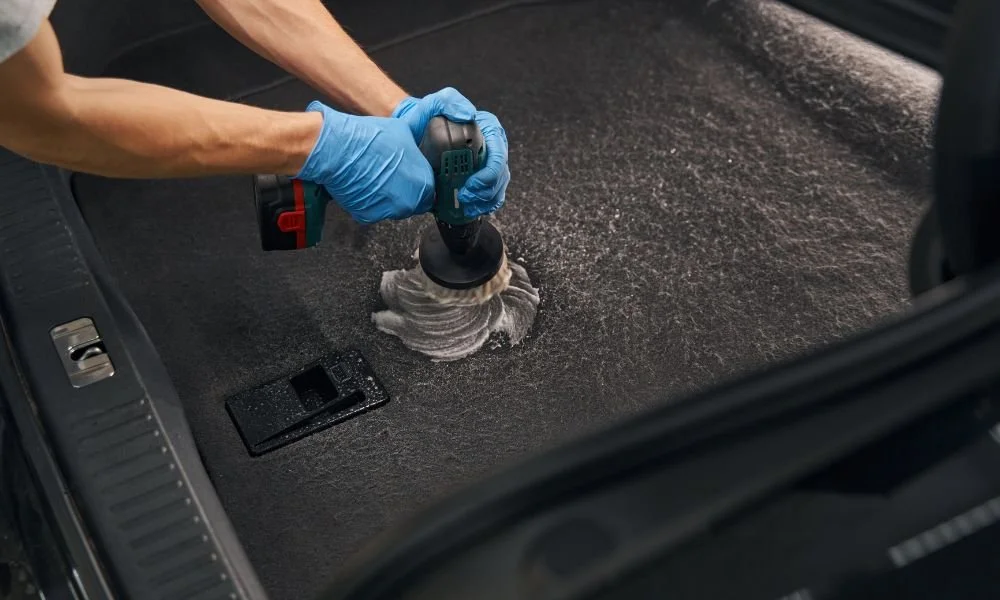Person using a power tool to clean car interior carpet, emphasizing auto detailing and vehicle maintenance.