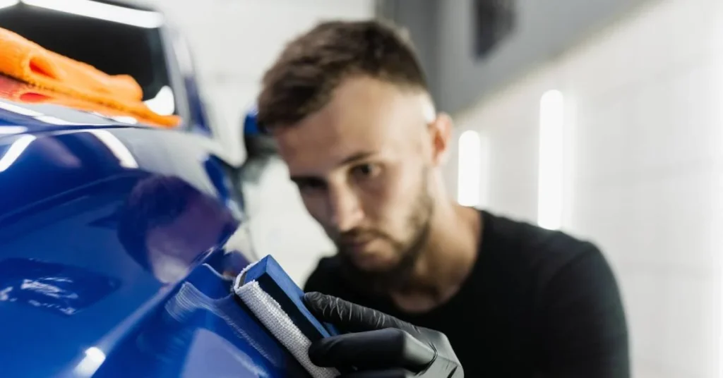 Man detailing a blue vehicle using a polishing pad, with an orange microfiber cloth nearby, emphasizing precision in auto detailing.