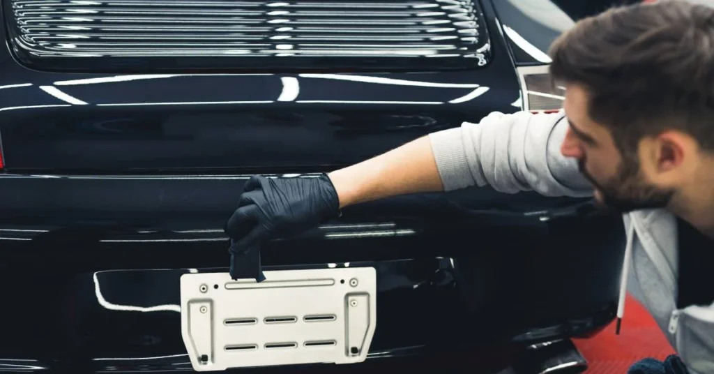 Man applying ceramic coating to the rear of a black vehicle, emphasizing automotive detailing and paint protection services in Omaha.