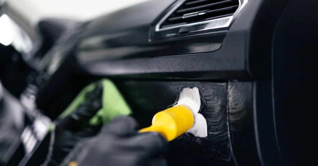 Professional car detailing process, cleaning dashboard with brush and cloth, enhancing vehicle appearance and protection.