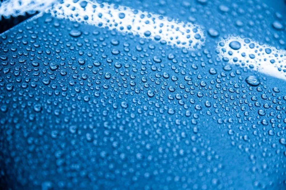 Close-up of water droplets on a blue car surface, illustrating the protective benefits of ceramic coating for vehicles in Omaha, NE's climate.