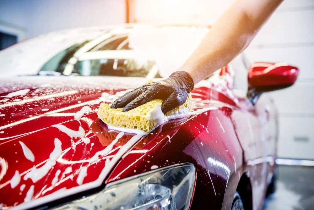 Person washing a red car with a sponge, demonstrating vehicle maintenance and care after paint protection film installation in Omaha, NE.