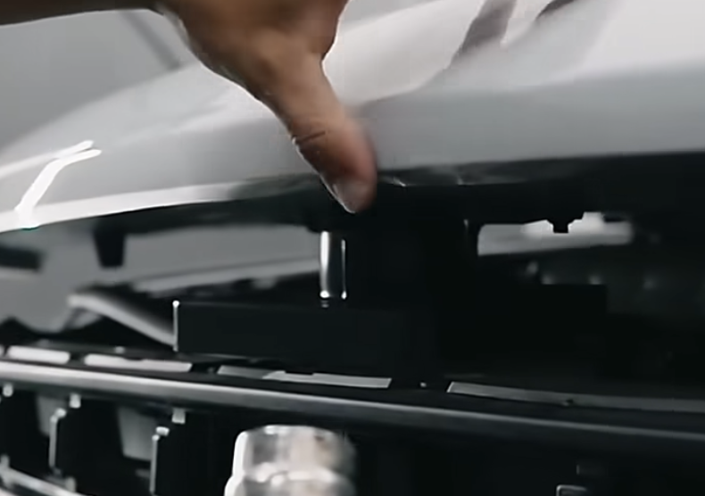 Hand adjusting a component under the hood of a vehicle, illustrating automotive detailing and maintenance for paint protection film installation.
