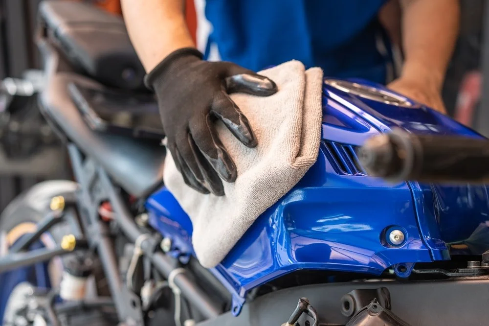 Person in gloves cleaning a blue motorcycle tank with a microfiber cloth, emphasizing motorcycle care and detailing services in Omaha.