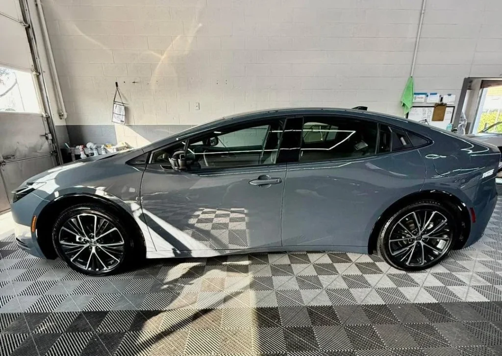 Gray vehicle in a detailing shop, showcasing paint protection film application, with a clean and polished exterior on a checkered floor.