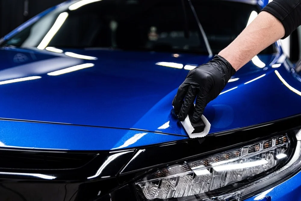 Person applying ceramic coating to a blue car hood, emphasizing automotive detailing services in Omaha, NE.