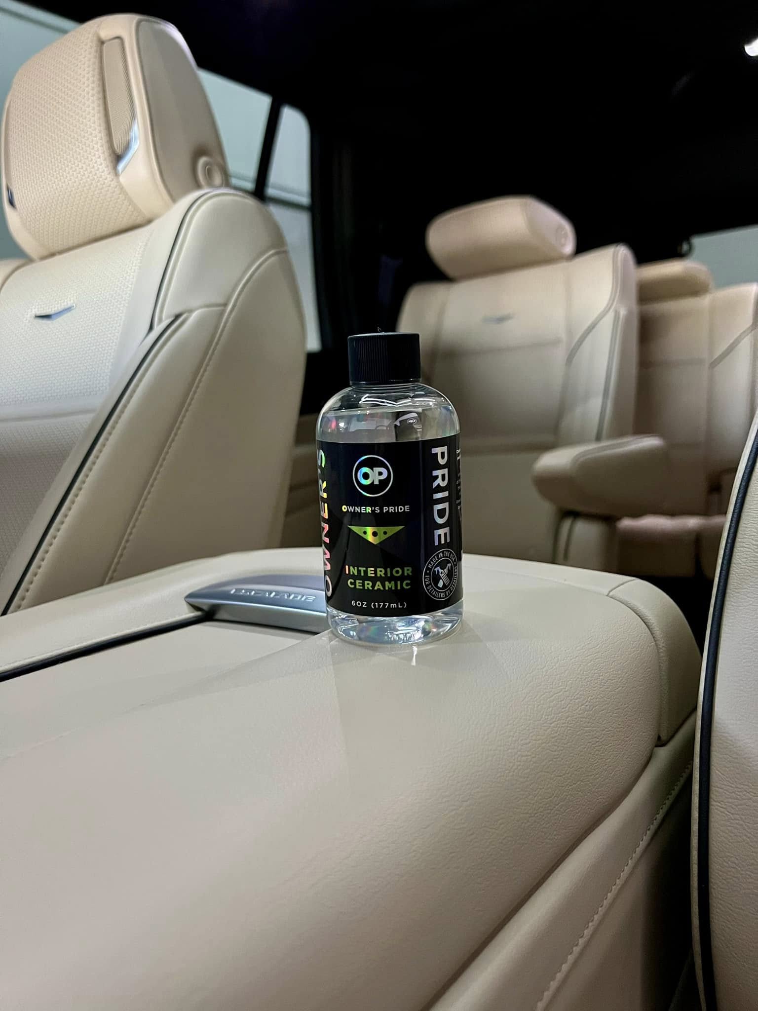 Bottle of Owner's Pride interior ceramic coating on a leather car armrest, showcasing premium vehicle protection for fabrics and surfaces.