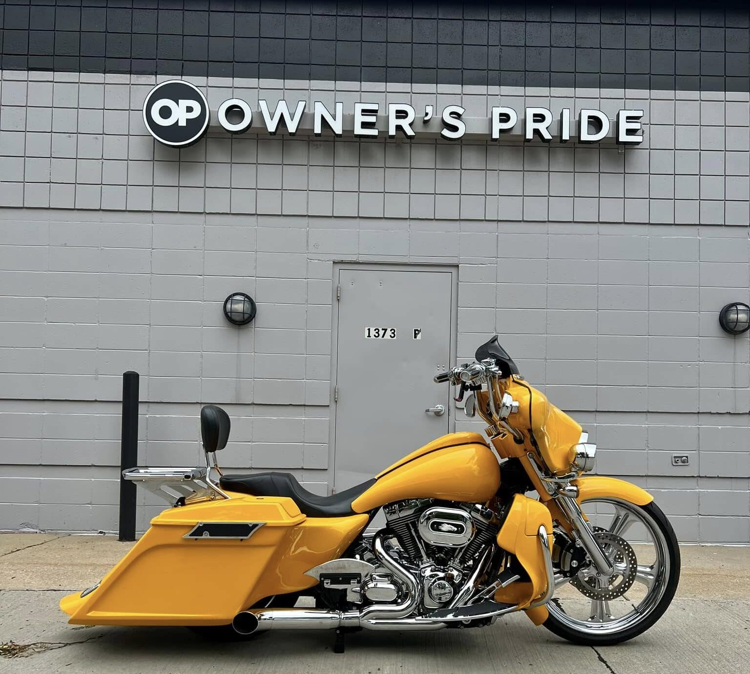 Yellow motorcycle parked in front of Owner's Pride building, showcasing ceramic coating benefits for motorcycle protection and aesthetics.