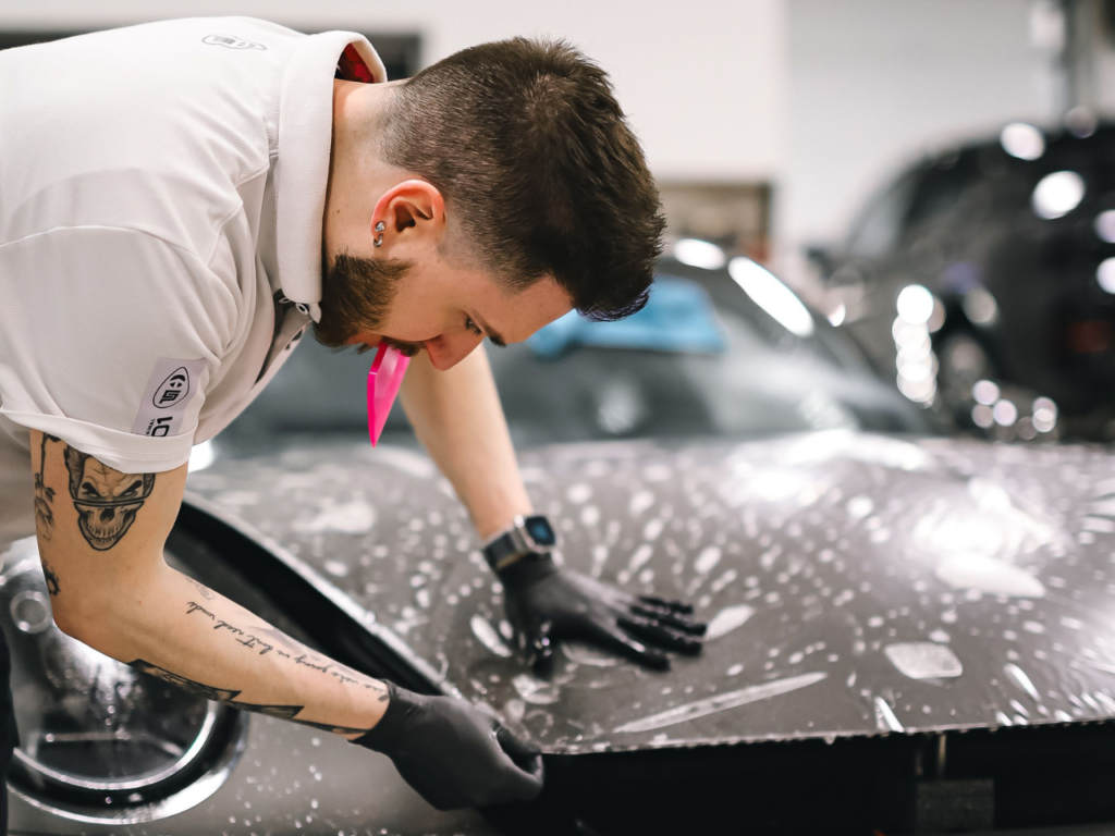 A technician carefully smoothing out paint protection film on a car's front end.